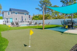 A backyard with artificial turf, a pool, lounge chairs, and a table with chairs.