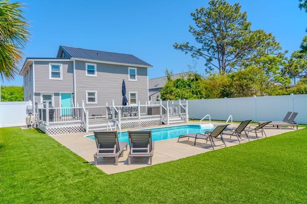 A two-story house with a swimming pool, a deck with chairs, and a fenced yard.