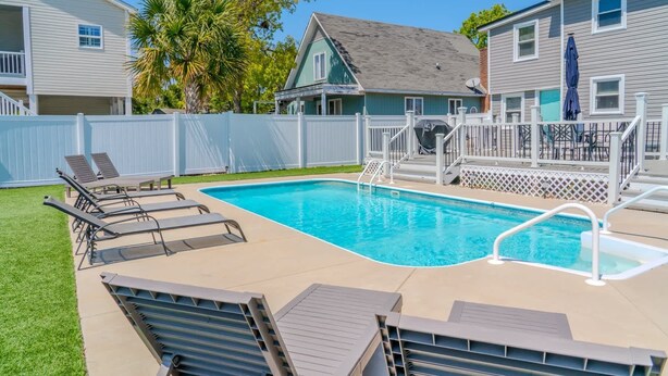 Piscina com espreguiçadeiras, área cercada e deck coberto.