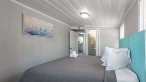 Une chambre d’hôtel avec un lit, un tableau, une salle de bain visible à travers une porte ouverte et un luminaire au plafond.