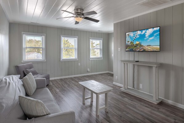 A living room with a sofa, a table, a ceiling fan, and a TV mounted on a wall.