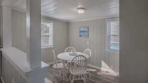 Un coin repas avec une table et des chaises blanches, un luminaire au plafond et un tableau accroché au mur.