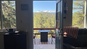 A cabin entrance with a 'Welcome to Cabin' sign, a dining table with chairs, a couch, and a view of a forest and mountains. - HOT TUB ~ 31 Acres ~Bring ATVs/Border Nat'l Forest (Teller County)