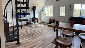 A cozy cabin interior with a spiral staircase, a wood-burning stove, a dining area with stools, and a 'Welcome to the Cabin' sign. - HOT TUB ~ 31 Acres ~Bring ATVs/Border Nat'l Forest (Teller County)