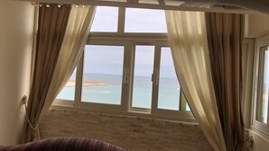 Una habitación con un ventanal grande que da a una playa, un muro de ladrillo y una cama con colcha a rayas.
