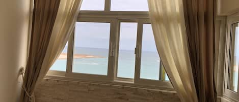 A room with a large window overlooking a beach, a brick wall, and a bed with a striped blanket.