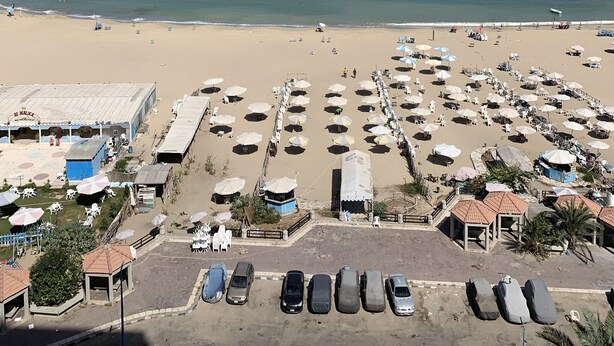 Una playa con muchas sombrillas y tumbonas, un aparcamiento y vistas al océano.
