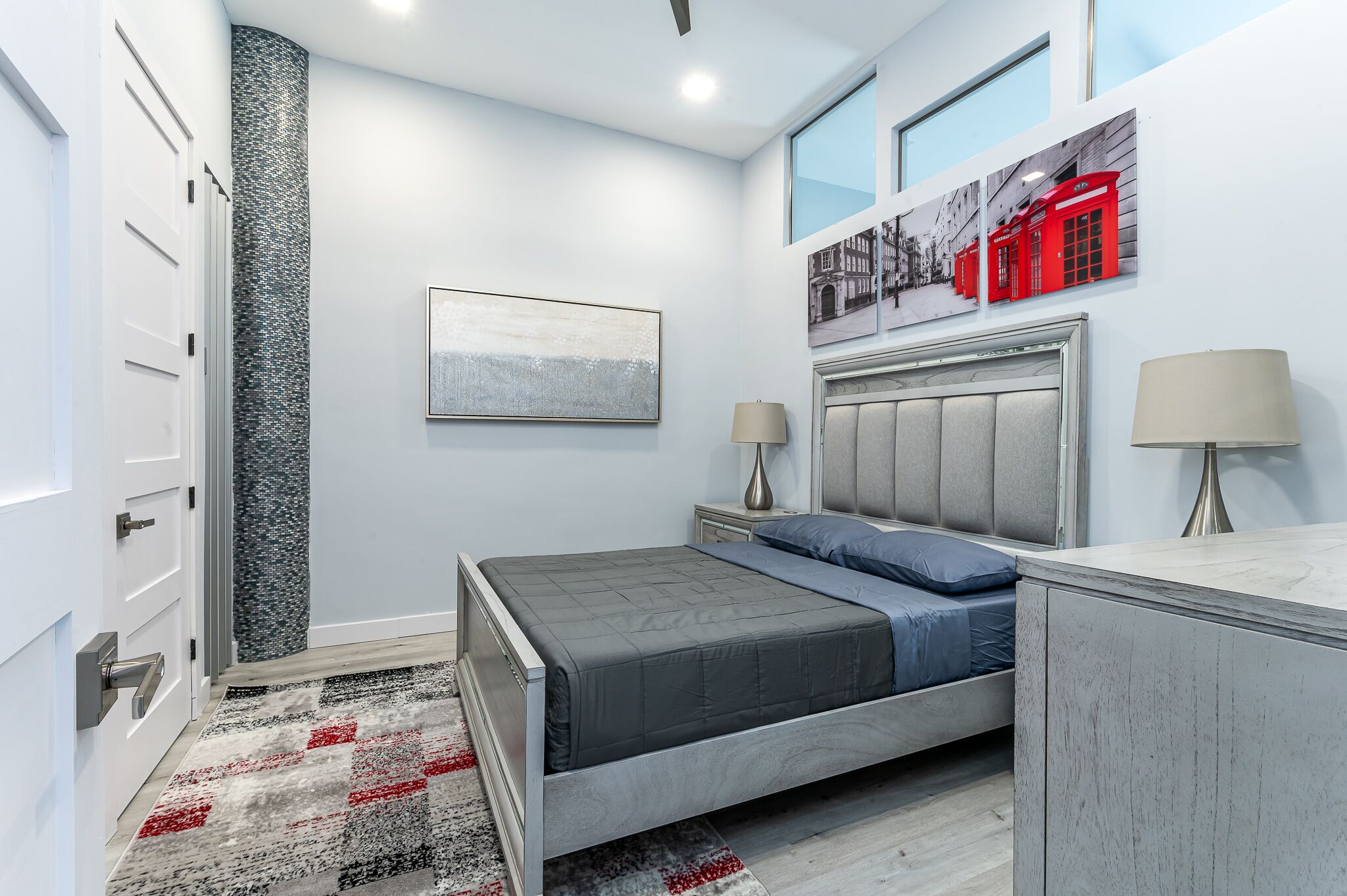 A modern bedroom with a bed, bedside lamps, a large window, and artwork on the wall.