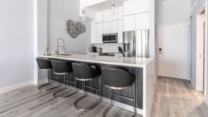 Una cucina moderna con isola centrale, sgabelli da bar, elettrodomestici in acciaio inossidabile e illuminazione a sospensione.