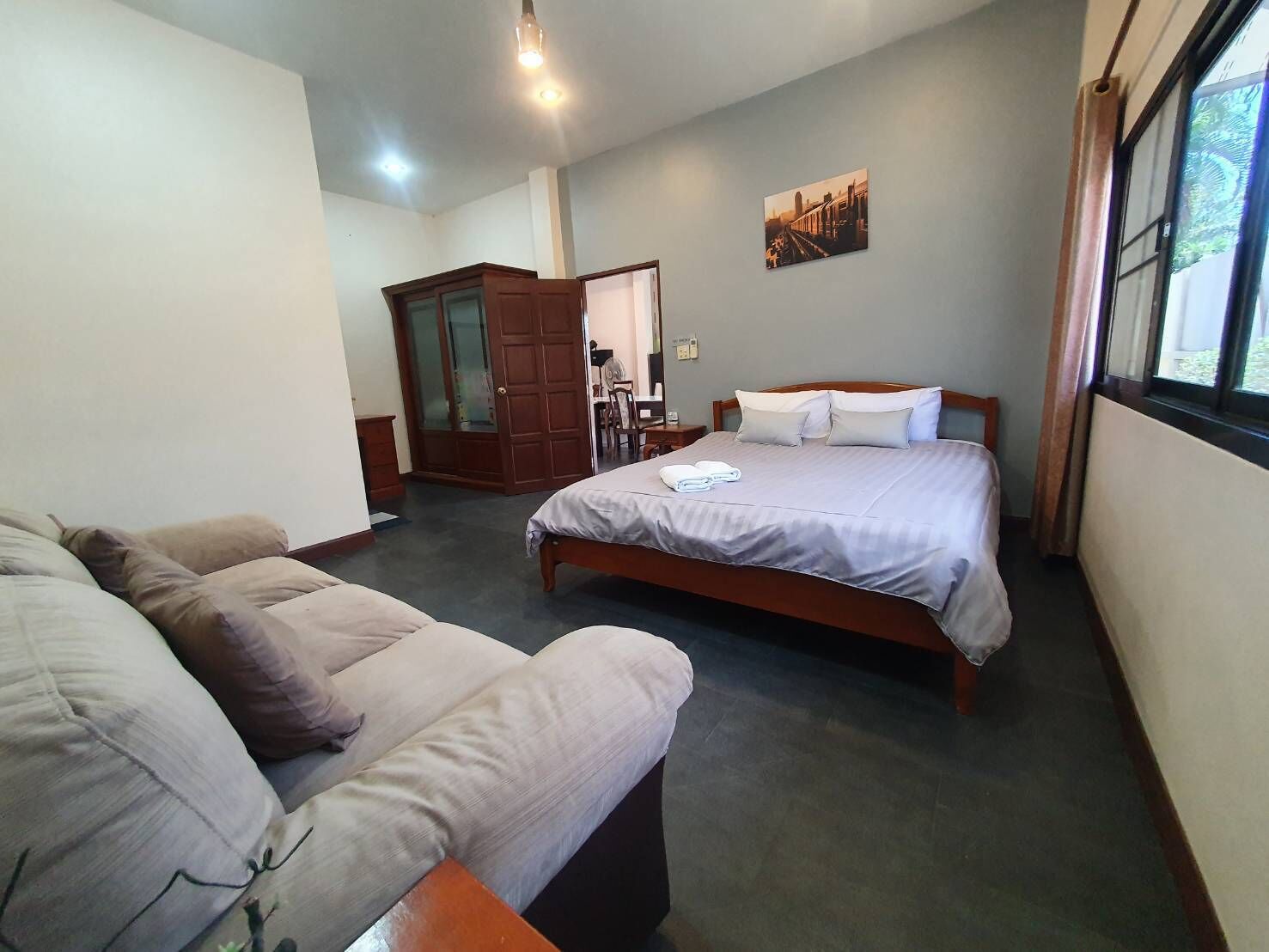 A hotel room with a bed, a sofa, a wardrobe, and a window.