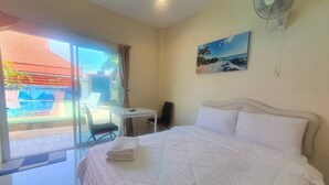 Ett hotellrum med en säng, ett skrivbord, en stol, en fläkt och en tavla på väggen.