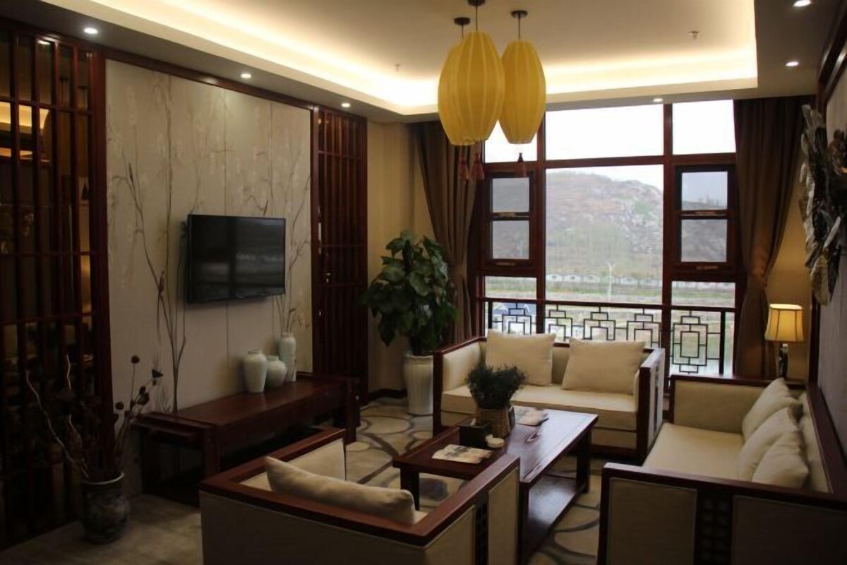 A modern living room with a sofa set, a coffee table, a TV mounted on the wall, and a large window with a view of a mountainous landscape.