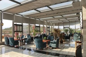 A spacious indoor area with a glass ceiling, multiple seating arrangements, and potted plants. - Yingzhigu Holiday Hotel (Mengyin)