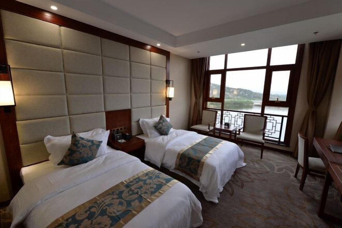 A hotel room with two beds, a large window with a view, a desk, and a chair.