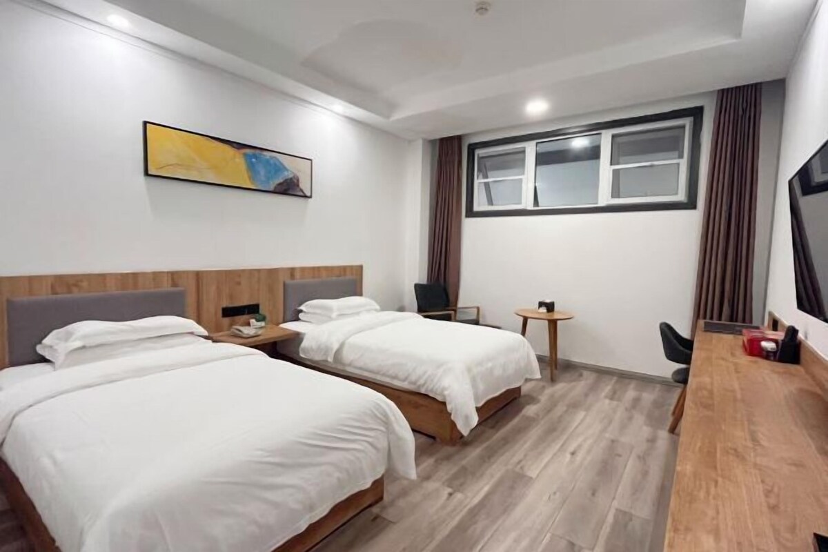 A hotel room with two beds, a desk, a chair, a TV, and a window with curtains.