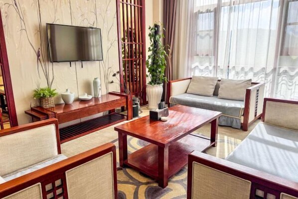 A modern living room with a sofa, coffee table, and chairs, a flat-screen TV mounted on the wall, and a potted plant. - Yingzhigu Holiday Hotel (Mengyin)