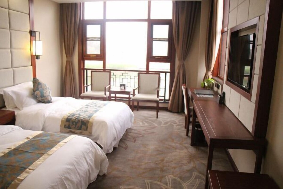 A hotel room with two beds, a desk, a chair, a TV, and a balcony with curtains.