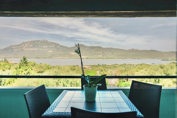 Un balcón con mesa y sillas, con vistas a un paisaje montañoso y una masa de agua.