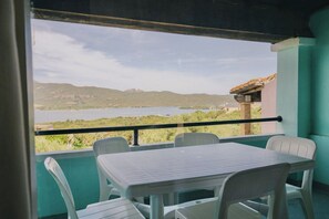 A balcony with a table and chairs, overlooking a body of water and hills. - Stella di Gallura: Two-room apartment for 4 people, air conditioning, Wi-Fi, ocean view (Porto Rotondo)