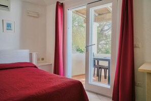 A bedroom with a bed, a sliding glass door to a balcony, and a small table with a chair. - Stella di Gallura Studio Apartment for 2 people, air conditioning, Wi-Fi, ocean view (Porto Rotondo)
