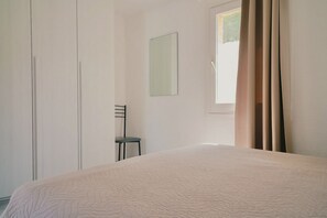 A bedroom with a bed, a chair, a mirror, and a window with curtains.