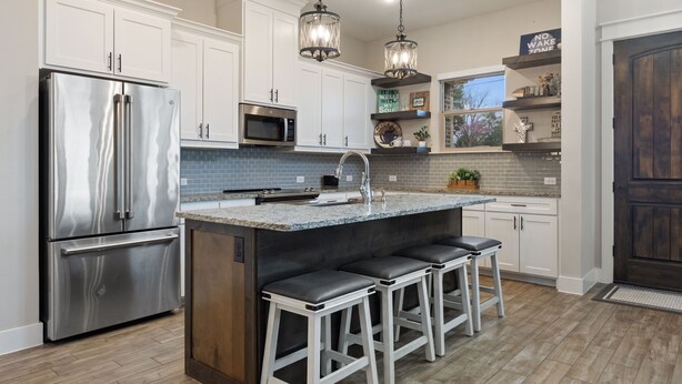 A modern kitchen with stainless steel appliances, white cabinetry, and a bar area with stools. - Miller's Cove on Lake Texoma! Luxury Lakeview Home! (Pottsboro)