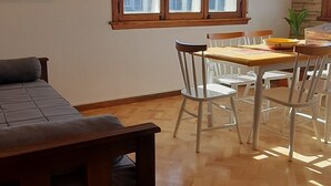 Ett rum med ett trägolv i fiskbensmönster, ett matbord med stolar, ett fönster med utsikt över byggnader och en tavla på väggen.