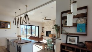 A modern kitchen with a central island, a dining area with a green chair, and a fireplace.