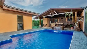 A swimming pool with a waterfall feature, a covered patio with outdoor seating, and a stone wall with a framed picture. - The Lake Village, La Fortuna de San Carlos (La fortuna)