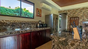 A kitchen with granite countertops, dark wooden cabinets, a stainless steel refrigerator, and a stone backsplash. - The Lake Village, La Fortuna de San Carlos (La fortuna)