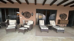 Ein überdachter Patio-Bereich mit Rattanmöbeln, darunter Stühle und eine Liege, sowie ein Boden aus Steinplatten.