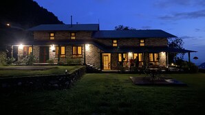 Una casa de piedra con múltiples ventanas y un porche, rodeada por un área verde.