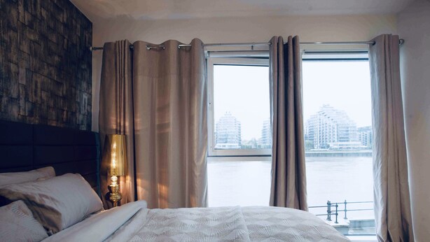 Une chambre d’hôtel avec un grand lit, une table de chevet avec une lampe et une vue sur une rivière et des bâtiments.