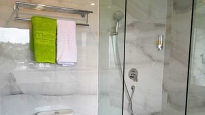 A modern bathroom with a glass-enclosed shower, a toilet, and a towel rack with two towels. - MaxOneHotels.com at Jayapura (Jayapura)