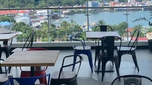 A restaurant with a view of a city and water. Tables and chairs are arranged inside. - MaxOneHotels.com at Jayapura (Jayapura)