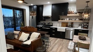 Une cuisine moderne avec des meubles noirs, un coin repas avec une table et des chaises en bois, et un salon confortable avec un canapé et une cheminée.