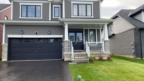 A two-story house with a garage, a front porch with a white railing, and a well-maintained lawn. - Spacious ,comfy house less than 15 mins drive to Niagara Falls and Outlet Mall. (Thorold)