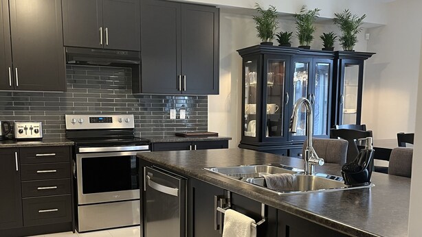 A modern kitchen with dark cabinetry, stainless steel appliances, and a built-in island with a sink. - Spacious ,comfy house less than 15 mins drive to Niagara Falls and Outlet Mall. (Thorold)