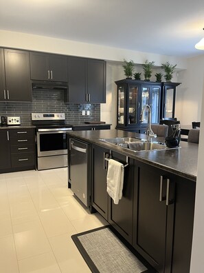 A modern kitchen with dark cabinetry, stainless steel appliances, and a built-in island with a sink. - Spacious ,comfy house less than 15 mins drive to Niagara Falls and Outlet Mall. (Thorold)