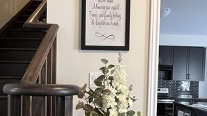A staircase with wooden handrails, a framed inspirational quote on the wall, and two vases with white flowers on a table. - Spacious ,comfy house less than 15 mins drive to Niagara Falls and Outlet Mall. (Thorold)