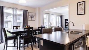 A modern kitchen with a central island, stainless steel appliances, and a dining area with black chairs and a table. - Spacious ,comfy house less than 15 mins drive to Niagara Falls and Outlet Mall. (Thorold)