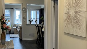 A hallway with a dark wood floor, a white door, and a large abstract painting on the wall. - Spacious ,comfy house less than 15 mins drive to Niagara Falls and Outlet Mall. (Thorold)