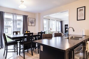 A modern kitchen with a central island, stainless steel appliances, and a dining area with black chairs and a table.