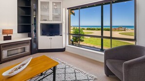 A living room with a large window, a flat-screen TV, a sofa, and a wooden table. - Gorgeous Beach and Ocean Views - Located right on the Beach and Pet Friendly! (Moana)