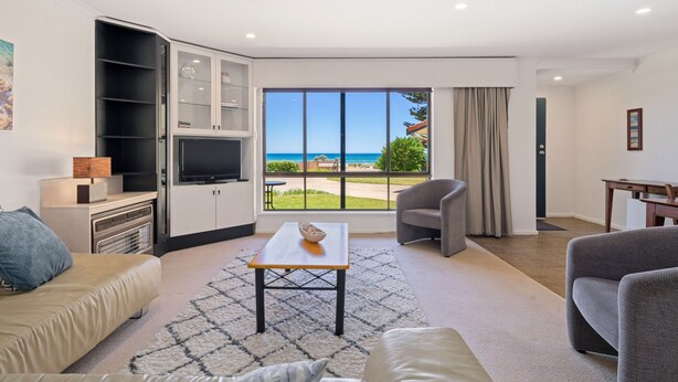 A modern living room with a large window, a flat-screen TV, a sofa, a coffee table, and a grey armchair. - Gorgeous Beach and Ocean Views - Located right on the Beach and Pet Friendly! (Moana)