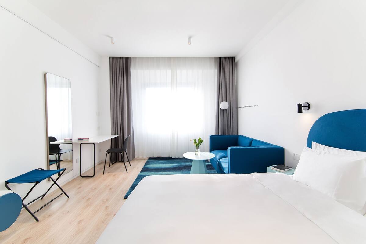 Een hotelkamer met een bed, een bureau, een stoel, een kleine tafel met een vaas en een blauwe bank.