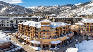 A multi-story hotel with a central courtyard, surrounded by snow-covered mountains. - Summer perfect private patio dining al-fresco walk out to pool golf hiking biking arts entertainment (Park City)