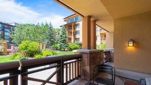 A balcony with a stone wall, a wooden railing, and a table and chair. - Summer perfect private patio dining al-fresco walk out to pool golf hiking biking arts entertainment (Park City)
