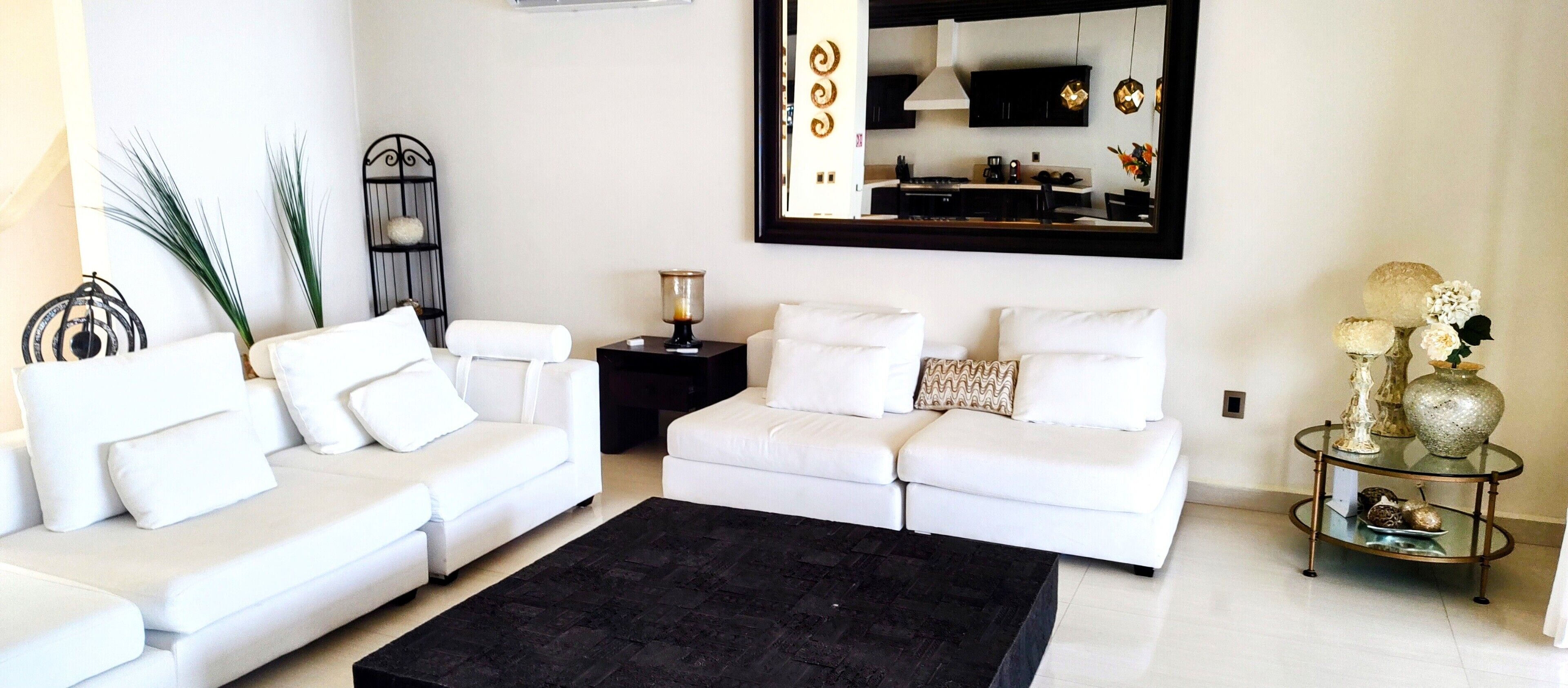 Una sala de estar moderna con un sofá blanco, un tapete negro y un espejo decorativo.