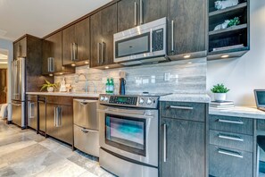 A modern kitchen with stainless steel appliances, dark wood cabinets, and a marble countertop.
